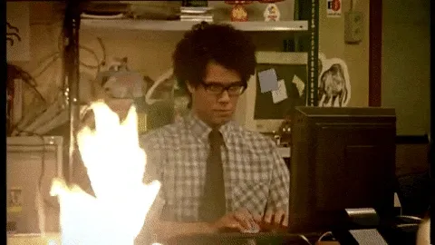 Gif from The IT Crowd TV show. Maurice sits at desk typing on computer while fire burns in foreground.